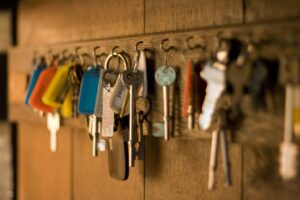 Rows of house keys with coloured tags hanging on hooks in a wooden key cabinet
