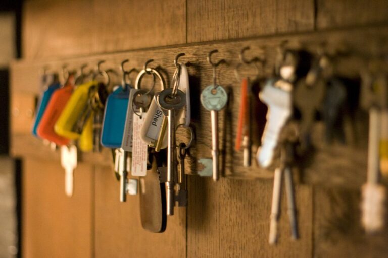 Rows of house keys with coloured tags hanging on hooks in a wooden key cabinet