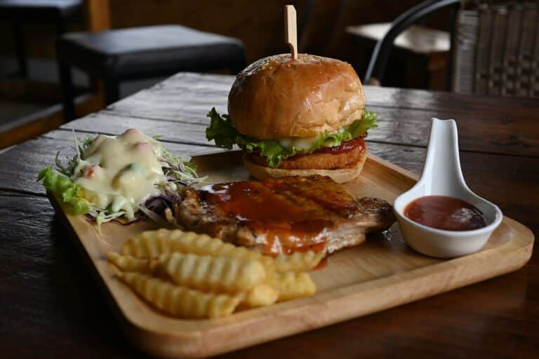A pub burger with lettuce and tomato served on a wooden board with crinkle-cut fries and dipping sauce