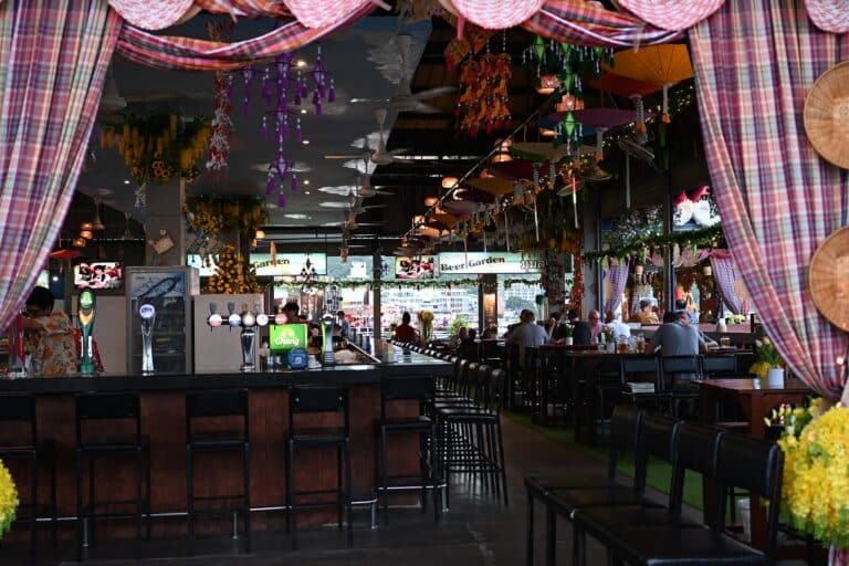 A relaxed open-air beer garden bar with high stools, hanging decorations and people enjoying evening drinks