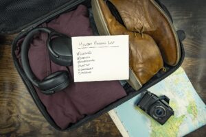 Open suitcase packed with clothes, boots, headphones, a camera and a handwritten holiday packing list