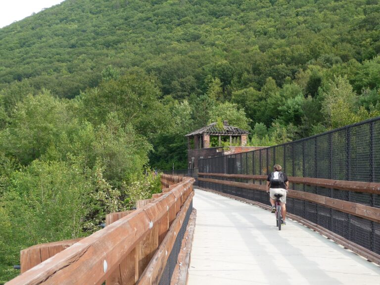 A cyclist crossing a wooden-decked bridge on the Lehigh Gorge rail trail with forested hillsides behind