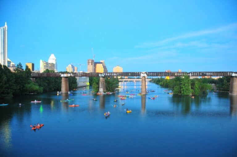 Kayakers and paddleboarders on Lady Bird Lake in Austin with the Congress Avenue bridge and downtown skyline behind
