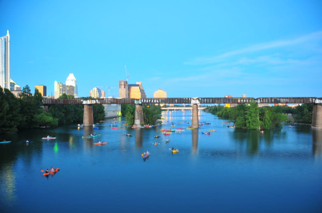 Kayakers and paddleboarders on Lady Bird Lake in Austin with the Congress Avenue bridge and downtown skyline behind