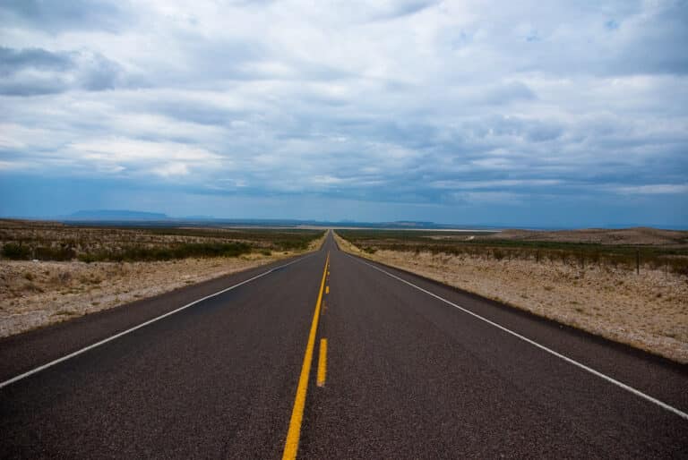 Long empty two-lane highway stretching to the horizon under a wide Texas sky