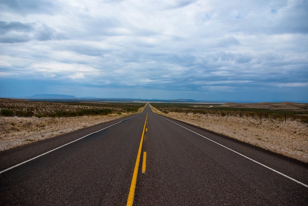 Long empty two-lane highway stretching to the horizon under a wide Texas sky