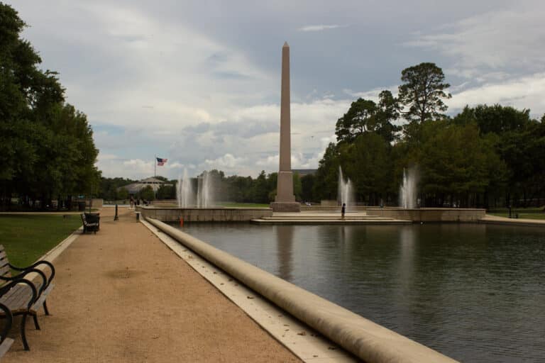 The reflection pool and Pioneer Memorial obelisk at Hermann Park, Houston, lined with live oaks on a sunny day