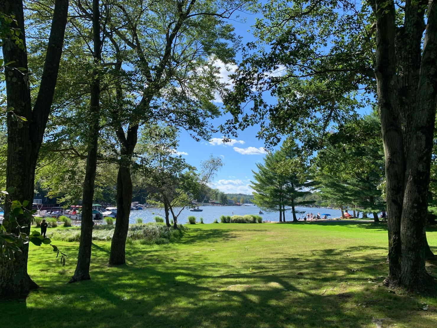 Lake Harmony, Pennsylvania seen through tall trees from a lakeside lawn on a sunny summer day, with boats on the water